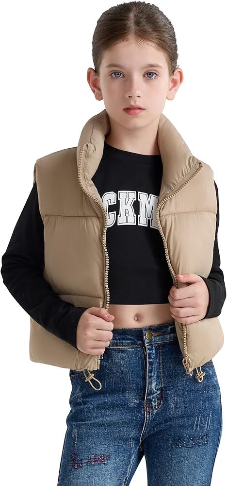 Nuori tyttö yllään beige toppaliivi, musta pitkähihainen paita ja farkut valkoisella taustalla.