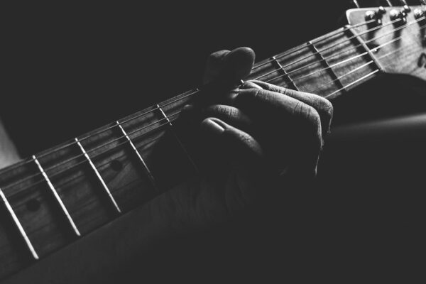 Lähikuva kädestä painamassa akustisen kitaran kieliä otelaudalla